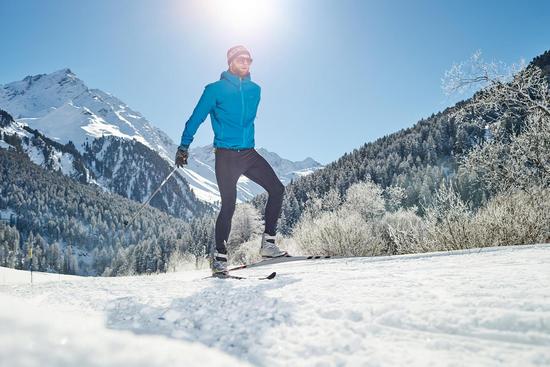 Ein Mann skatet mit Langlaufskin durch eine winterliche Landschaft im Sonnenschein